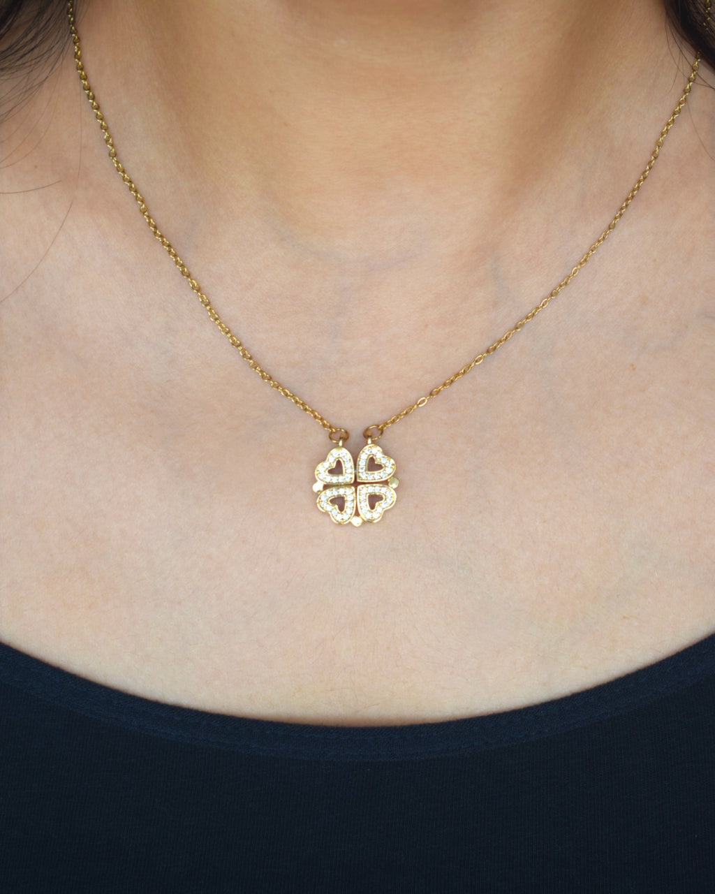 Gold necklace with a clover-shaped pendant worn by a person.