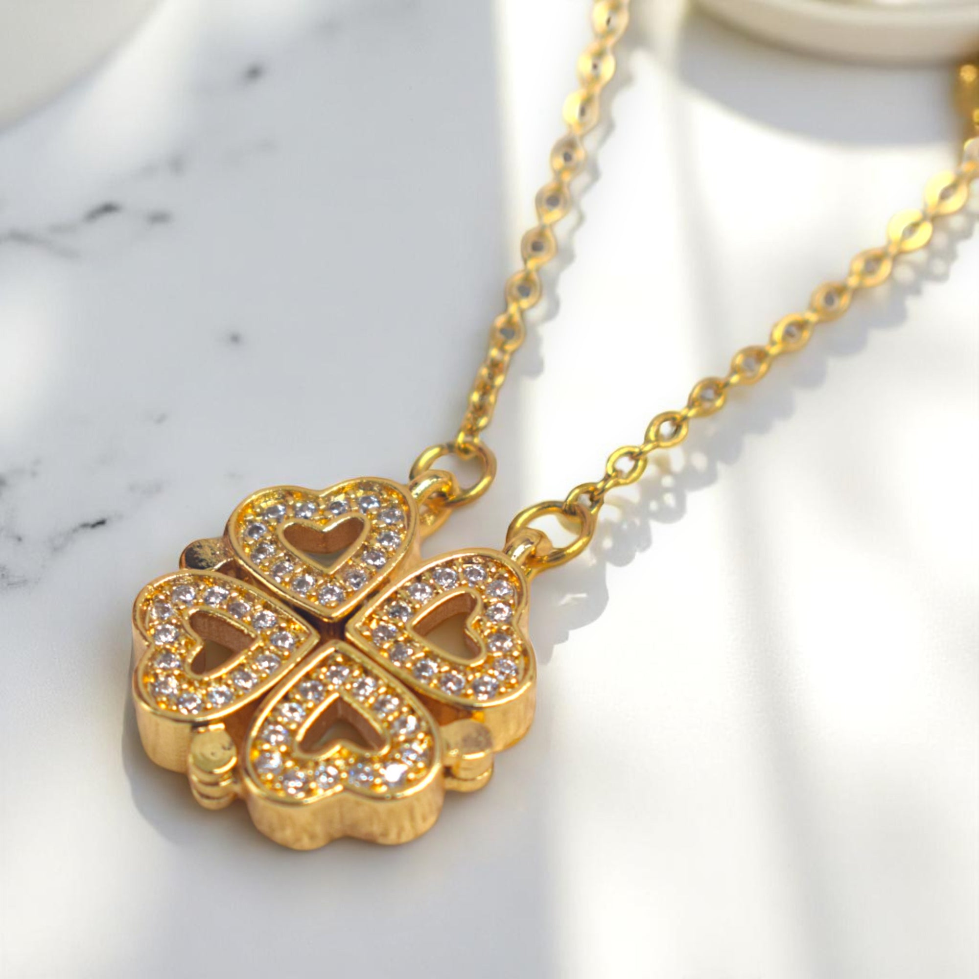 Gold necklace with a clover-shaped pendant on a marble surface