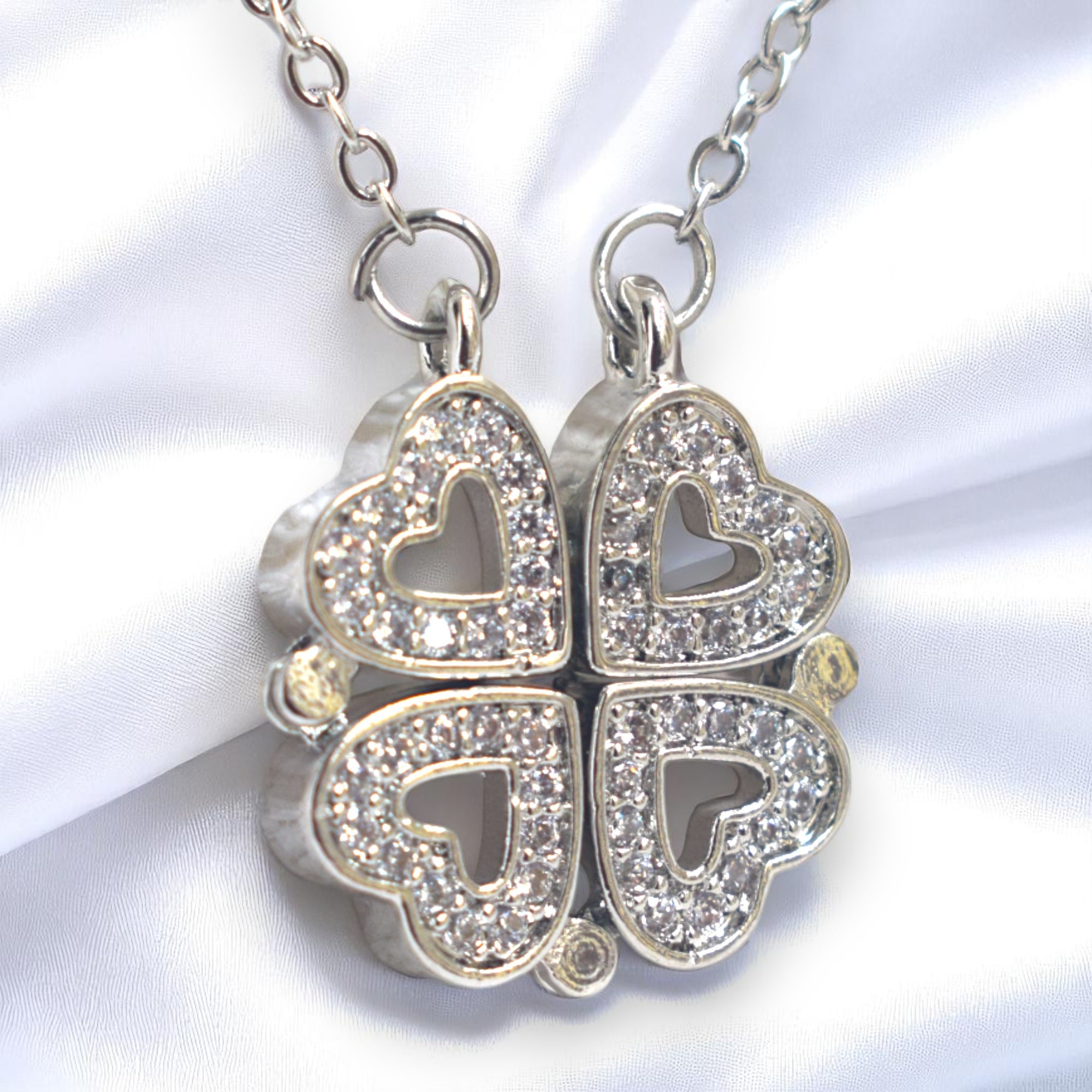 Silver four-leaf clover pendant with heart designs on a white fabric background