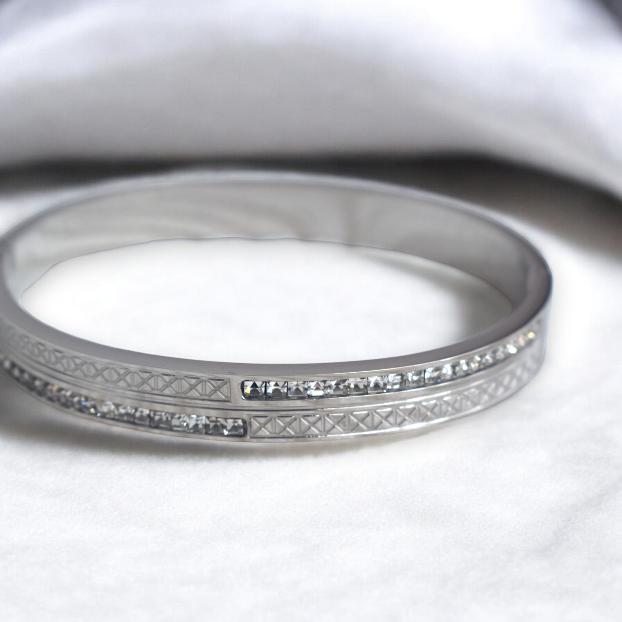 Diamond studded silver bangle on a white marble floor