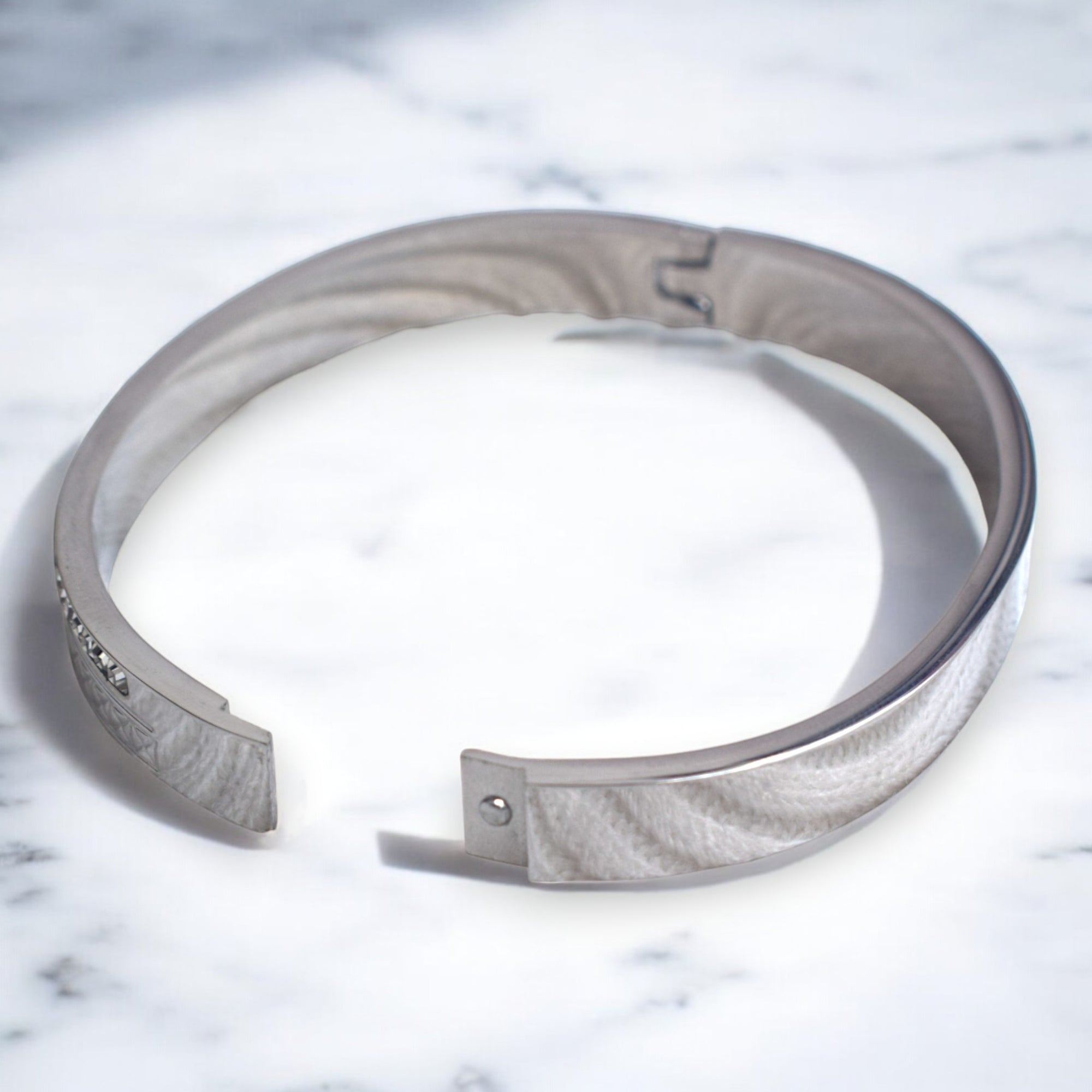 Diamond studded silver bracelet on a white marble floor