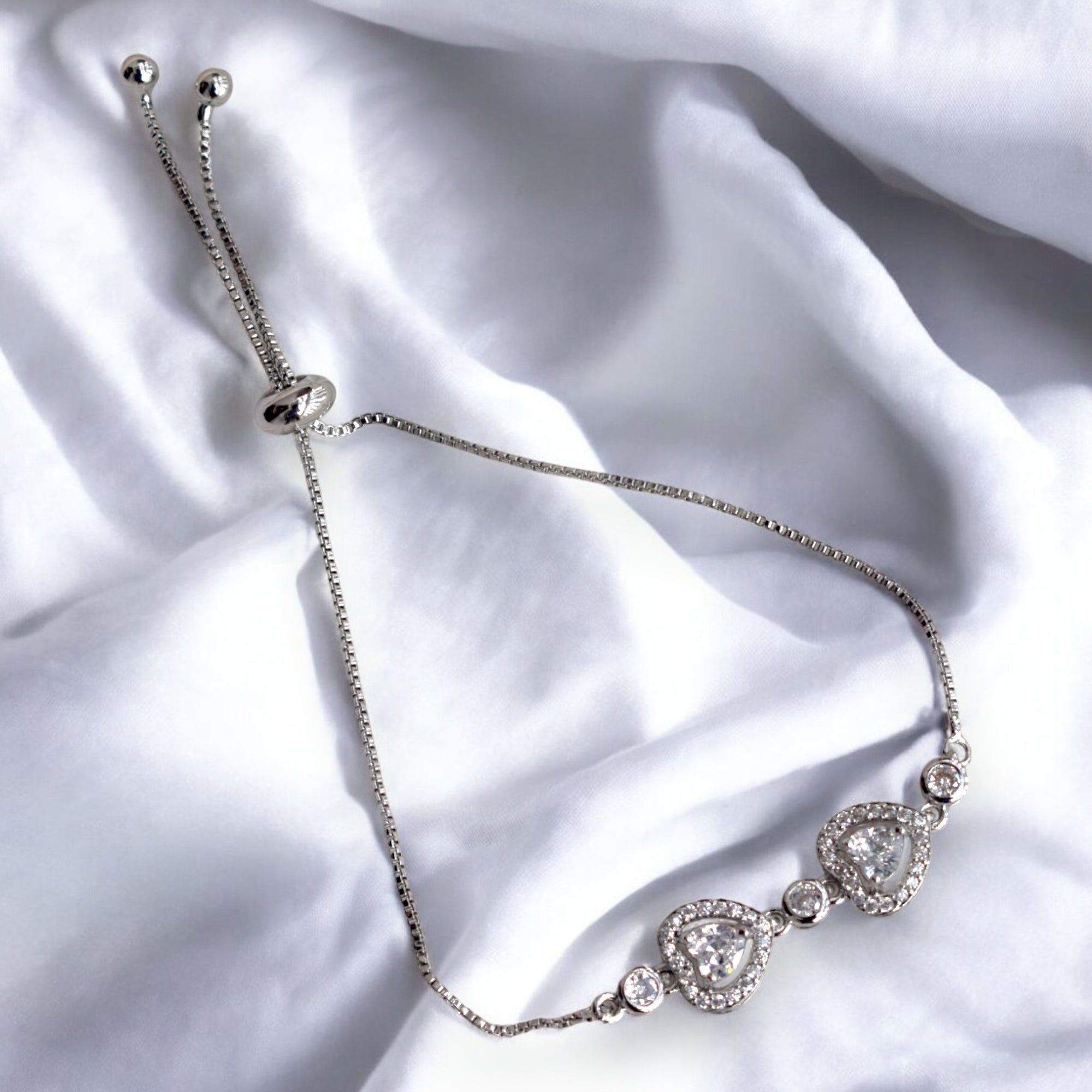 silver heart shaped diamond chain bracelet on a white satin cloth