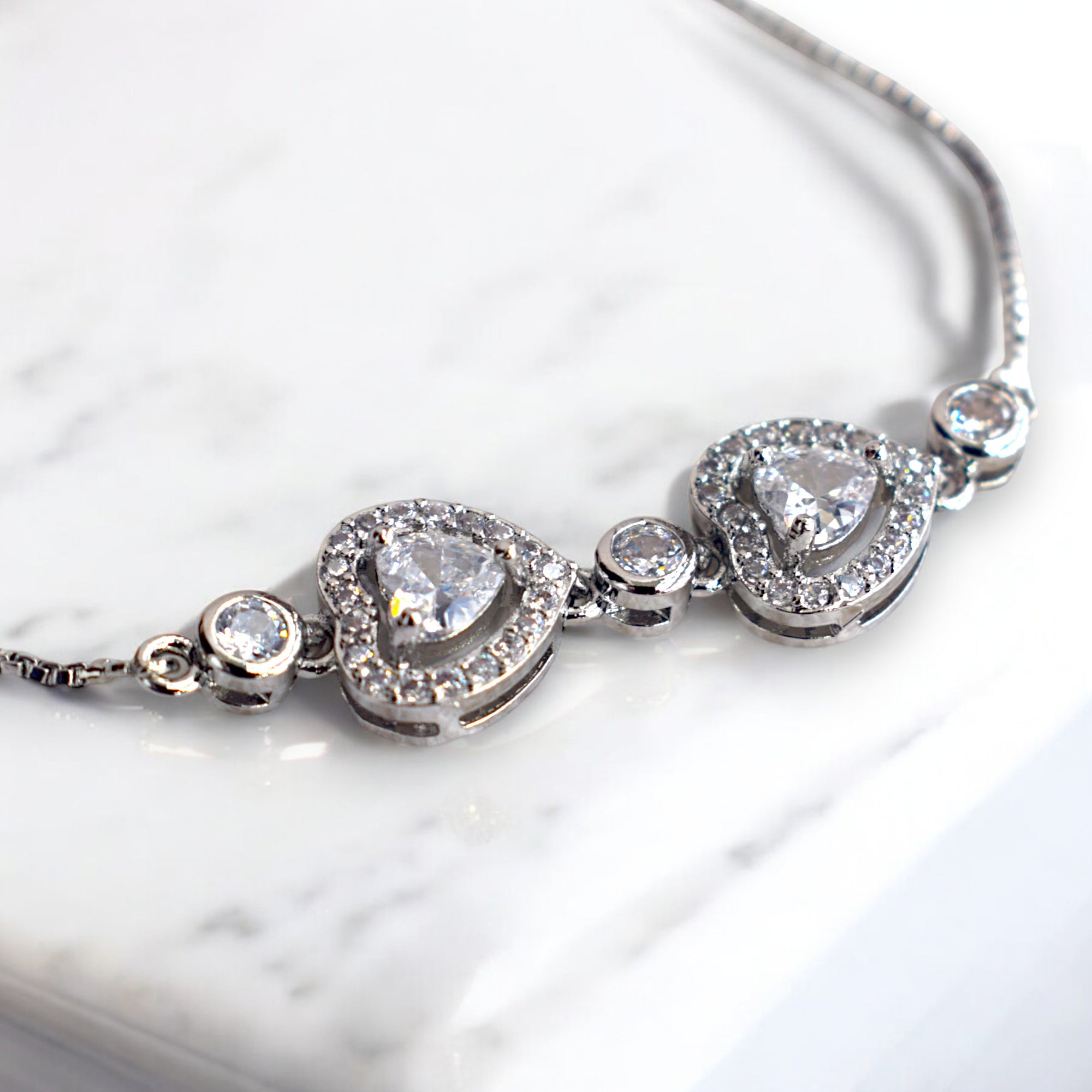 silver heart shaped diamond chain bracelet on a white marble floor
