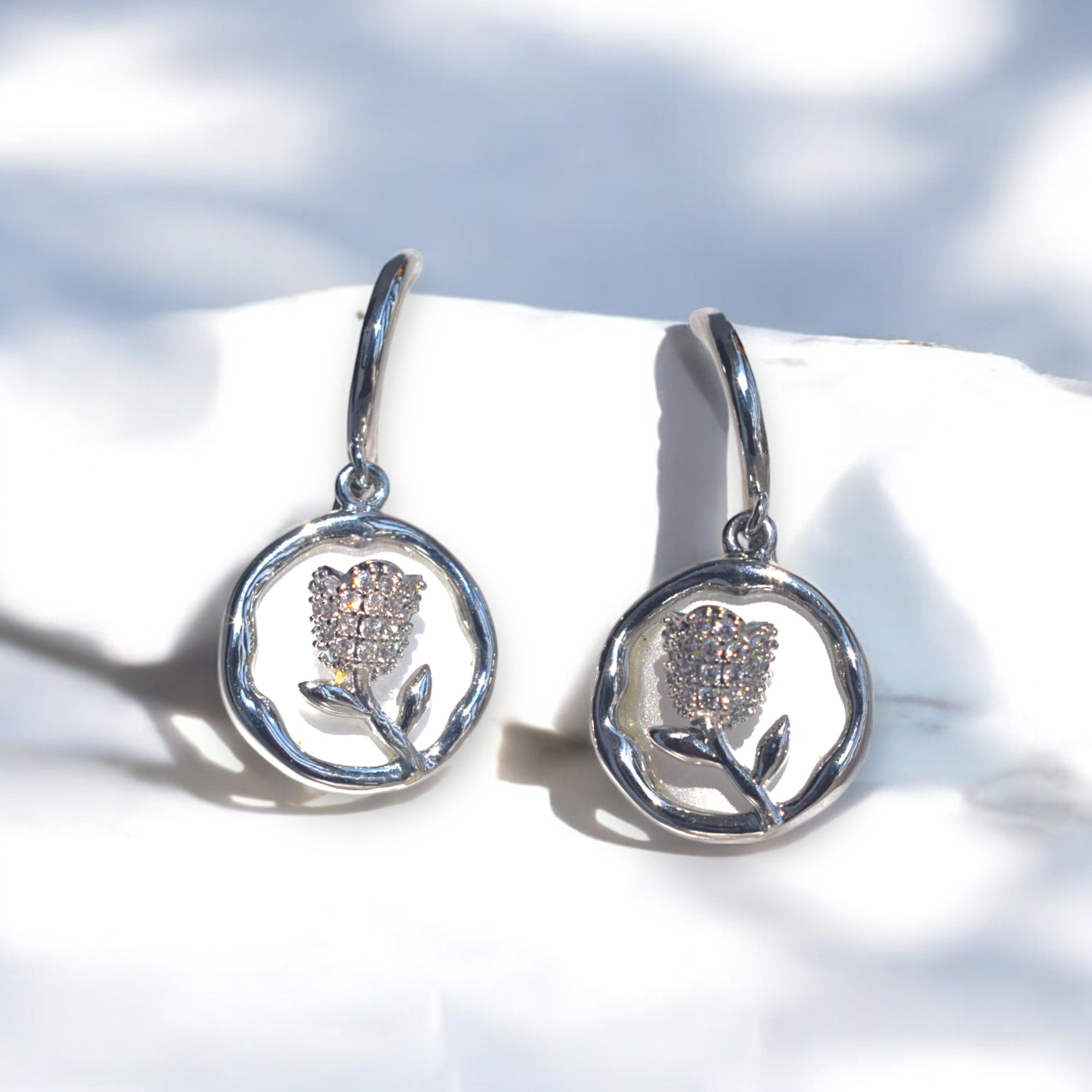 Silver round flower earrings with Zirconia stones placed on a white satin cloth