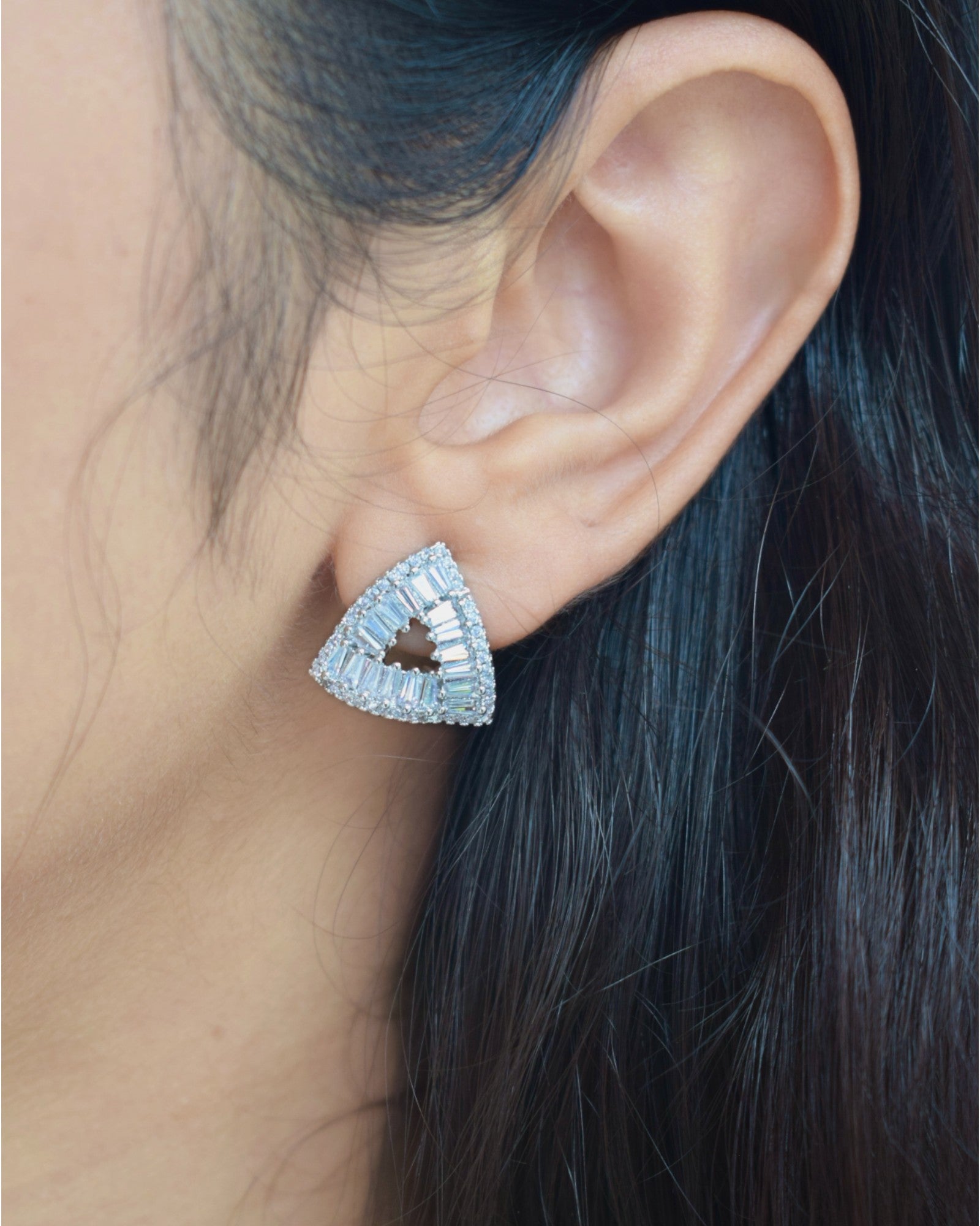 Triangular earrings worn by a person with dark hair.