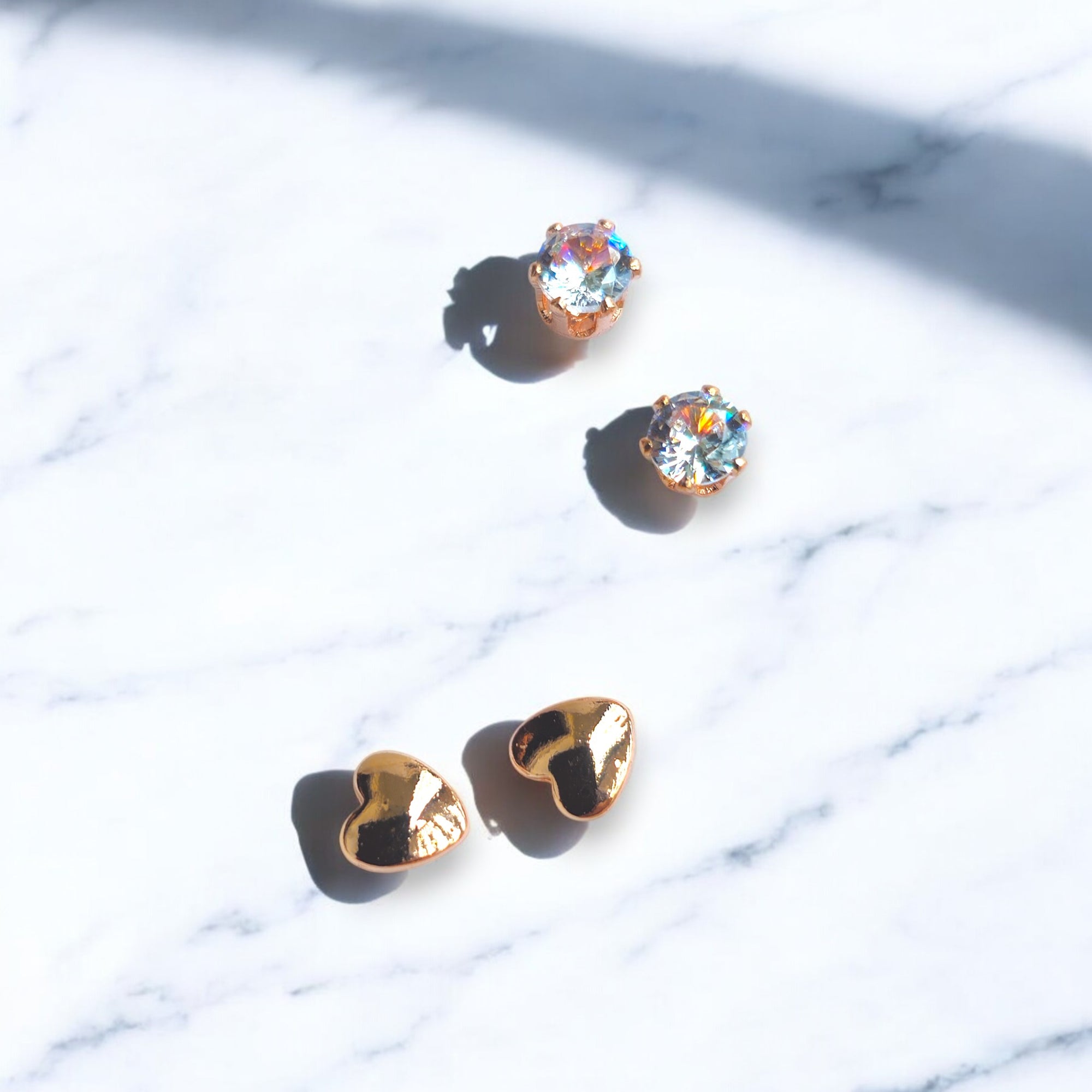 Rose gold zirconia crystal studs and heart shaped rose gold studs on a white marble floor