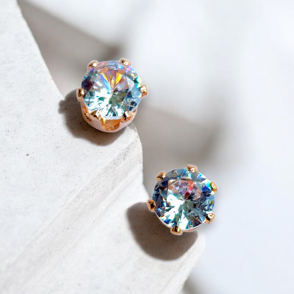 Rose gold earring with round Zirconia crystal studs on a white marble background 