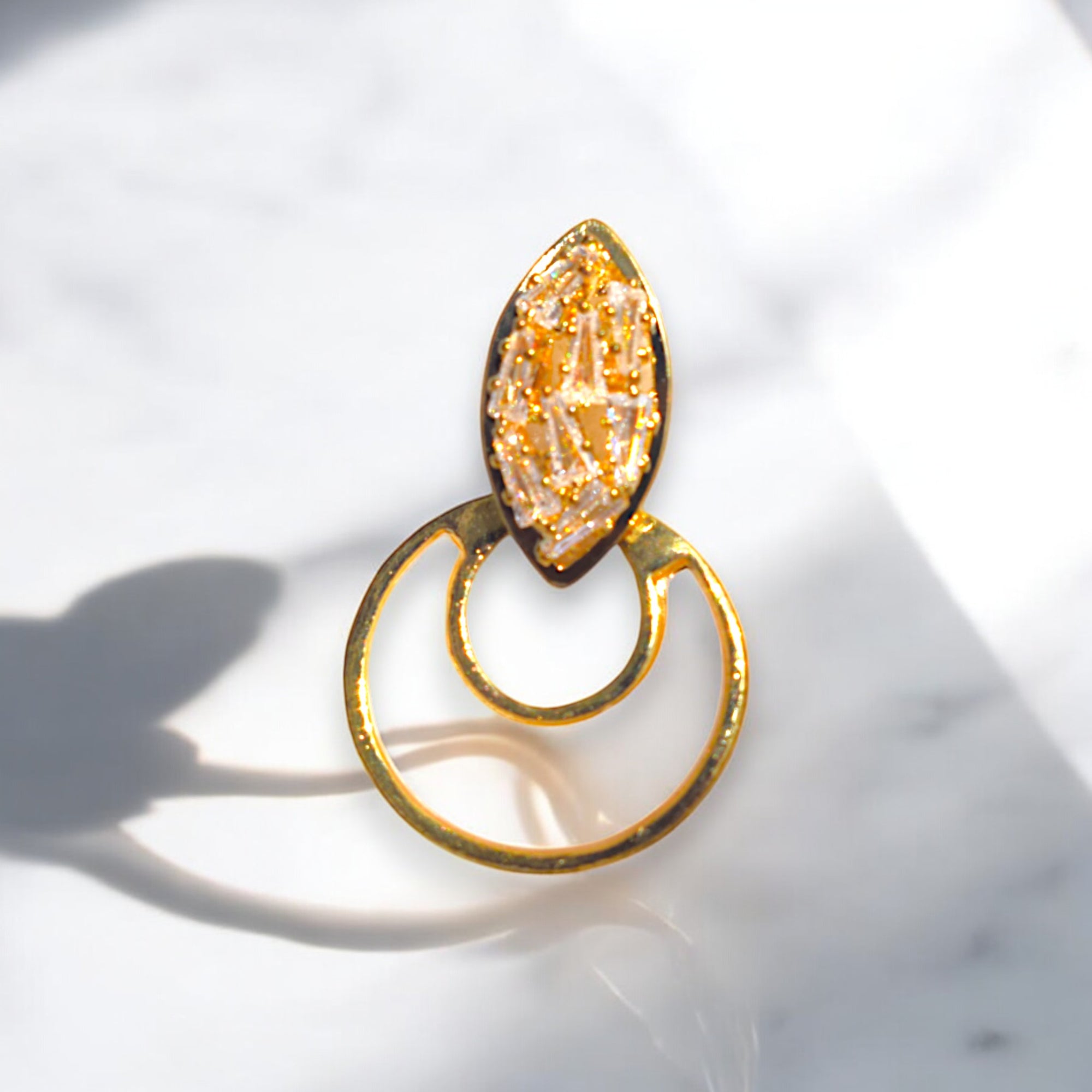 a single golden crescent moon zirconia stone studded earring on a white marble floor